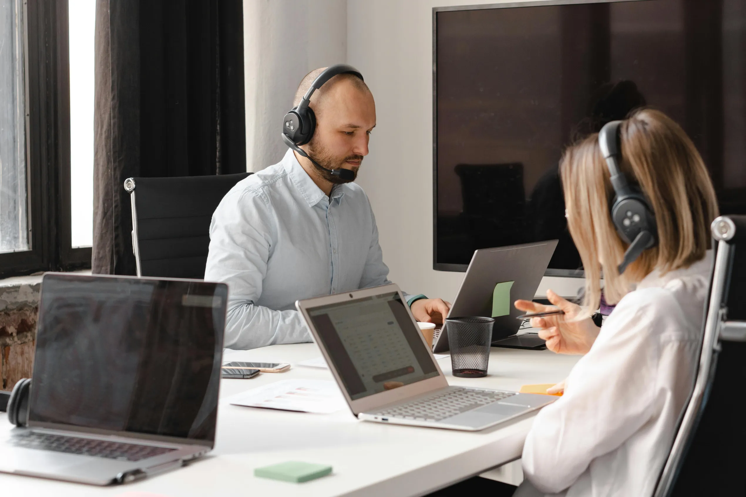 Berater sitzt am Telefon und eine weitere Beraterin ist in einem Video Call